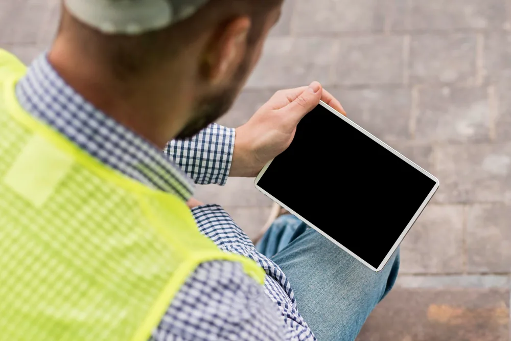 Person in a high-visibility vest reviewing an inspection checklist on a tablet at a job site.