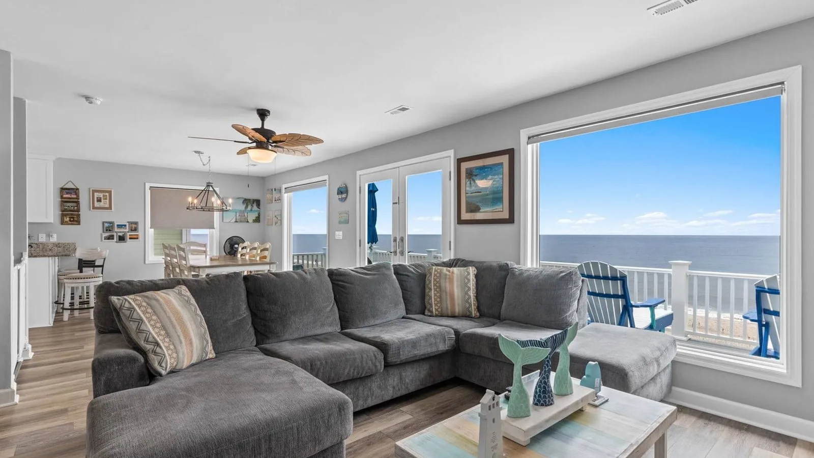 Clean, staged oceanfront living room with a gray sectional and a wide window looking out to the beach.