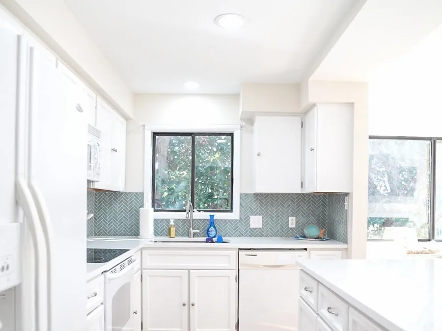 Renovated kitchen with white cabinets, white countertops, and a green herringbone tile backsplash.