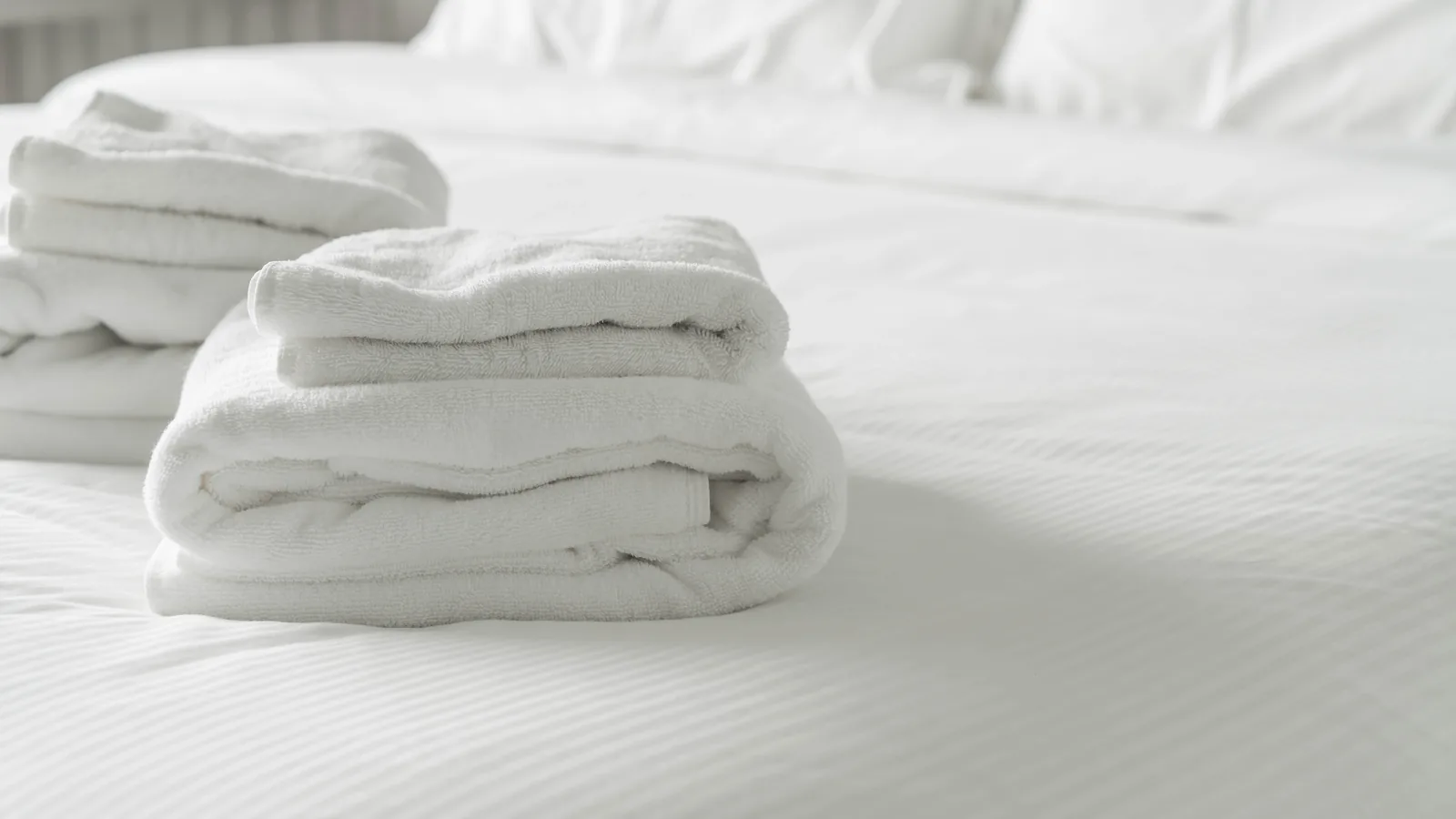 Folded white towels on a freshly made bed after a rental turnover clean.