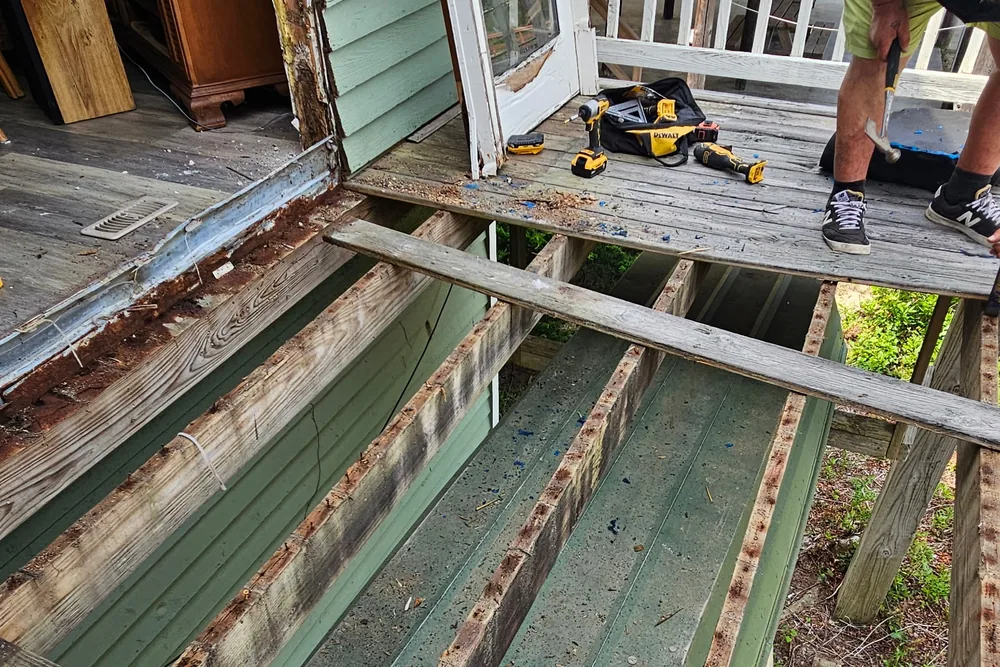 Deck repair in progress: boards pulled up to expose rotted joists, with drills and tools on the deck.