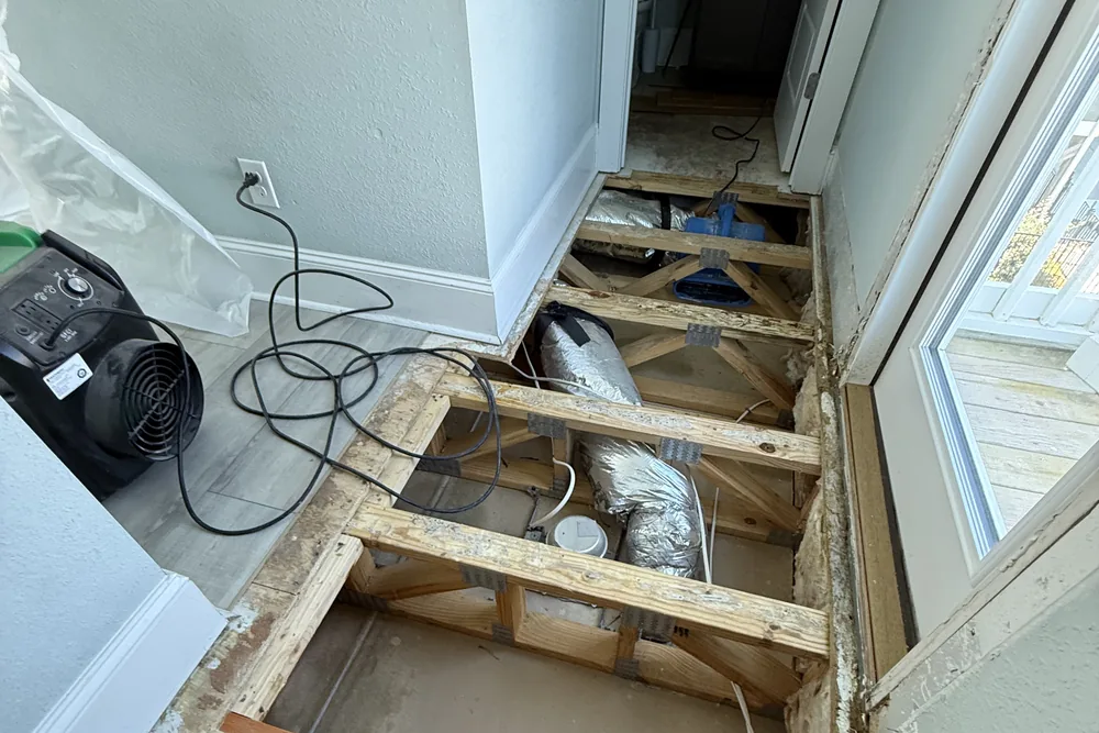 Water mitigation in progress: floor opened to the joists and ductwork, with an air mover drying the space.