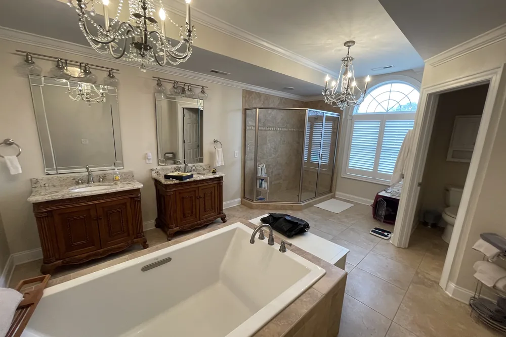 Before: master bath in Oak Island with a drop-in tub, dated wood vanities, and a corner shower, ahead of a full gut.