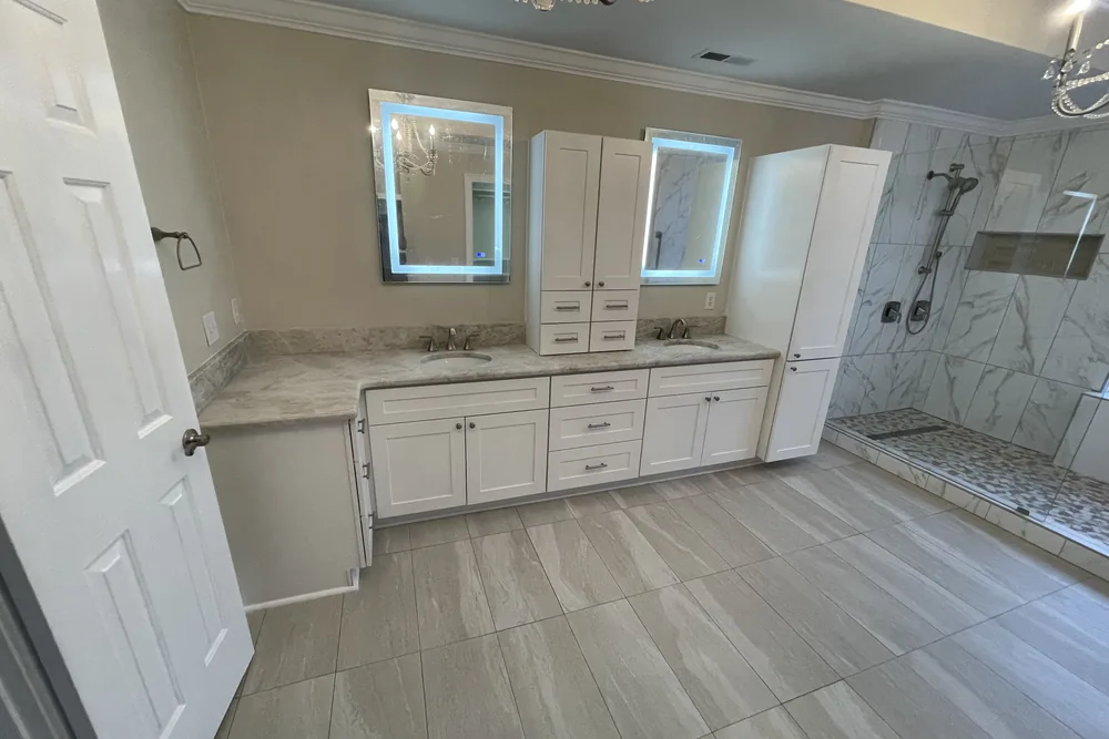 After: master bath gut in Oak Island, finished with a white double vanity, lighted mirrors, and a large tiled shower.
