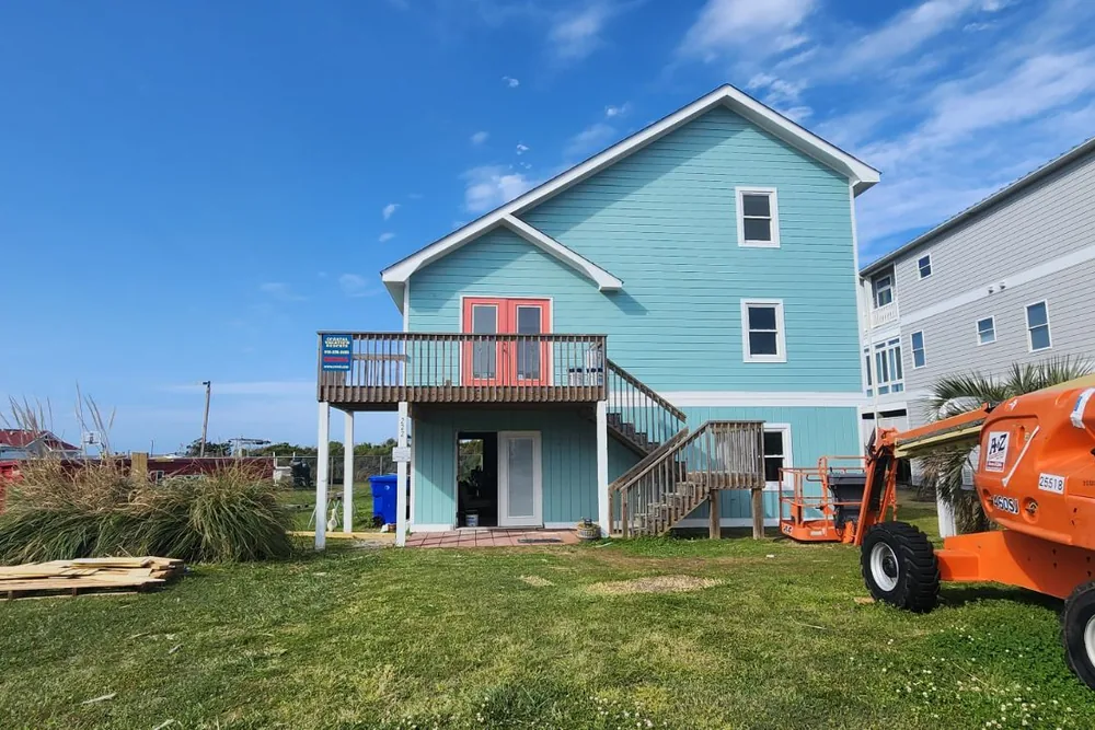 After: raised beach house in Caswell Beach finished in blue fiber cement siding, with new windows and white trim.