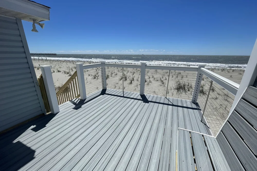 Oceanfront deck extension in Oak Island with composite boards and cable railing, overlooking the dunes and beach.