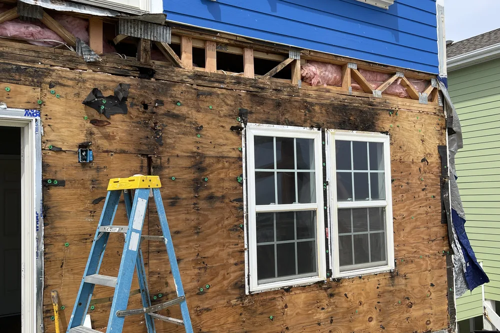 Before: exterior wall in Oak Island stripped to stained, damaged sheathing around a pair of windows.
