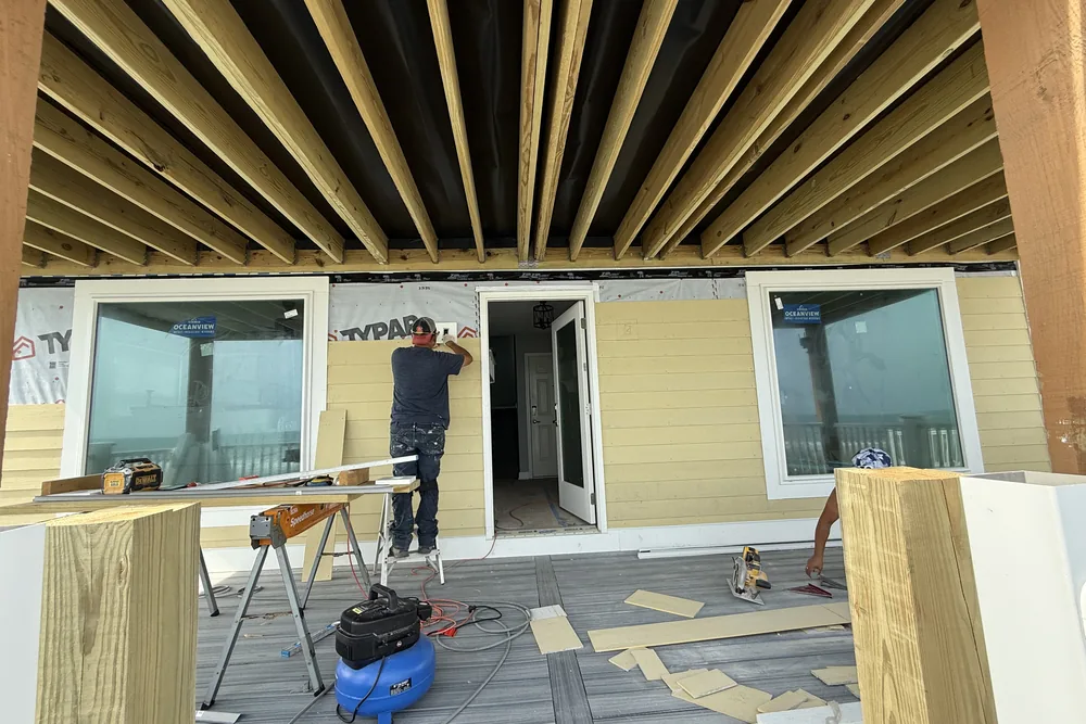 Envelope rebuild in progress in Oak Island: crew installing new lap siding over house wrap below a raised deck.