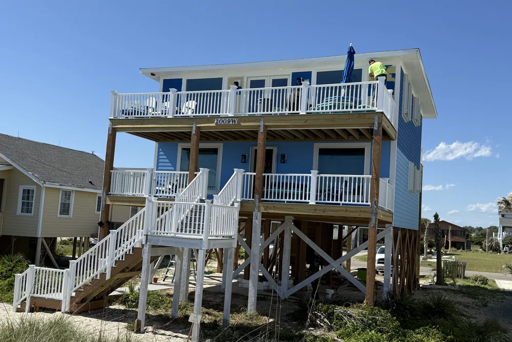 After: raised beach rental in Oak Island finished in blue siding, with white deck railings and stairs.