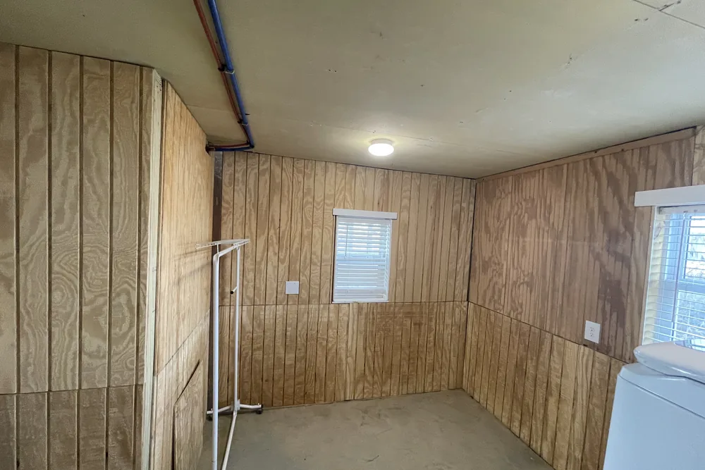 Before: bare ground-floor room in Oak Island with plywood walls and a concrete floor, ahead of the suite conversion.
