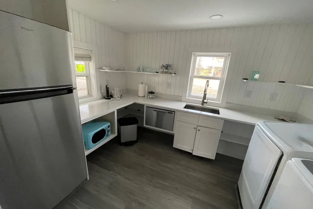 After: new kitchenette in Oak Island with white cabinets and counters, a stainless fridge, sink, and dishwasher.