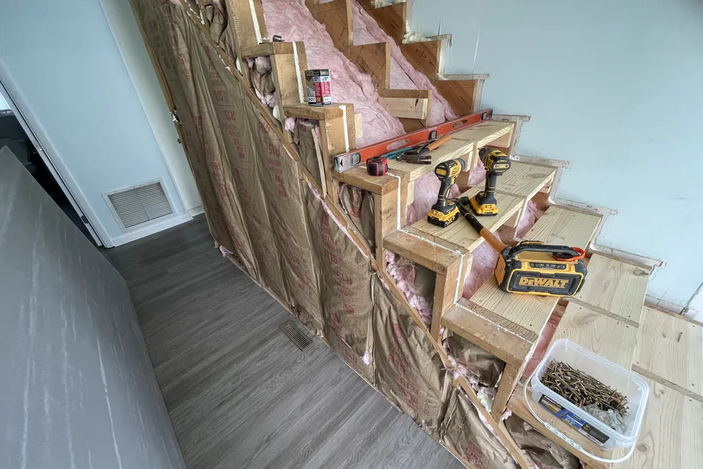 Stair rebuild in progress in Oak Island: framing shored and insulated, with drills and a level on the steps.