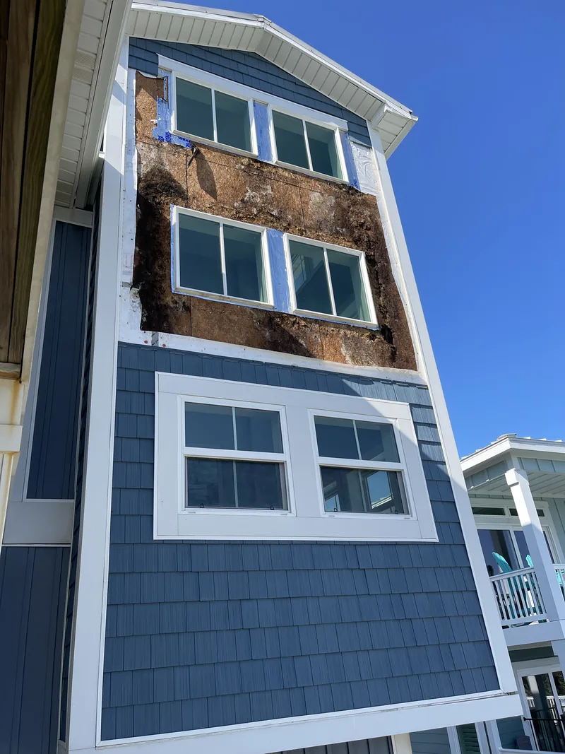 Wall rebuild in Oak Island: siding stripped from the upper floors of a three-story home, exposing the sheathing.