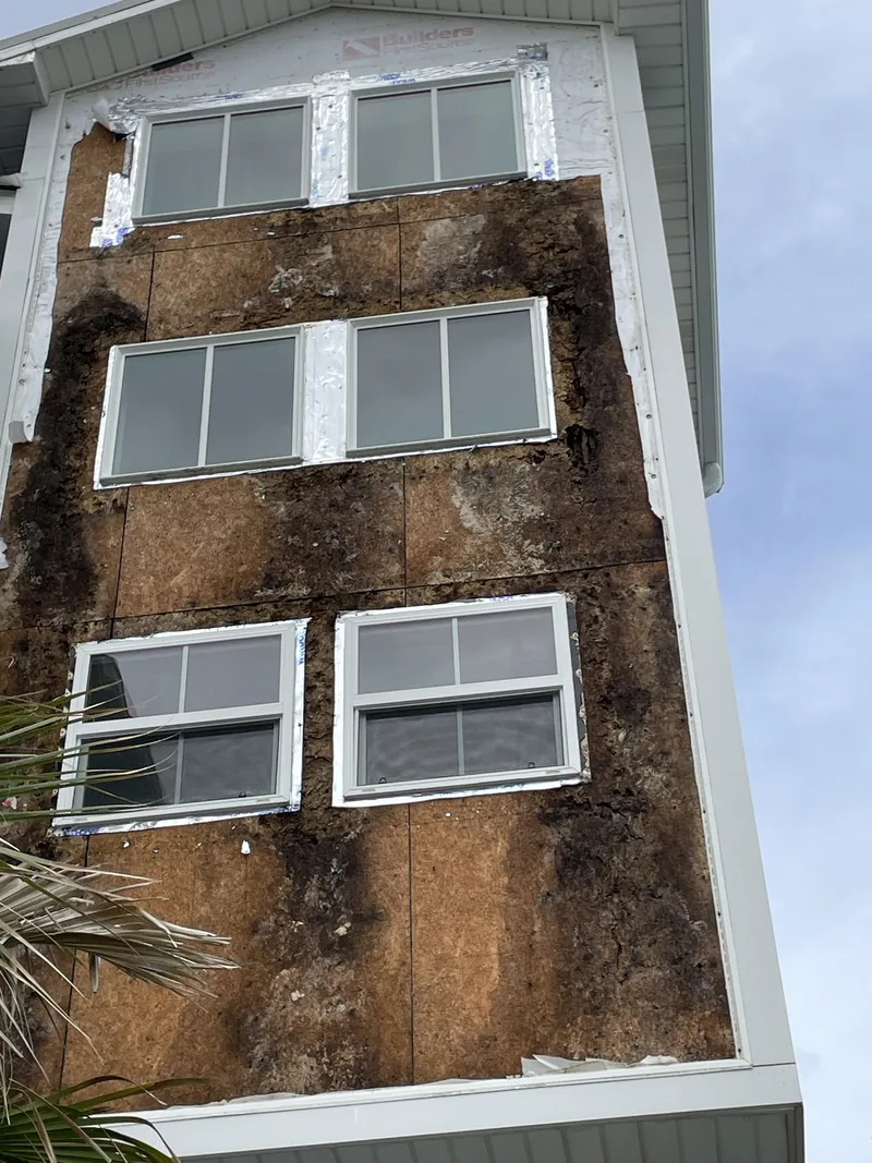 Stained sheathing exposed across three stories in Oak Island after the siding came off for a wall rebuild.